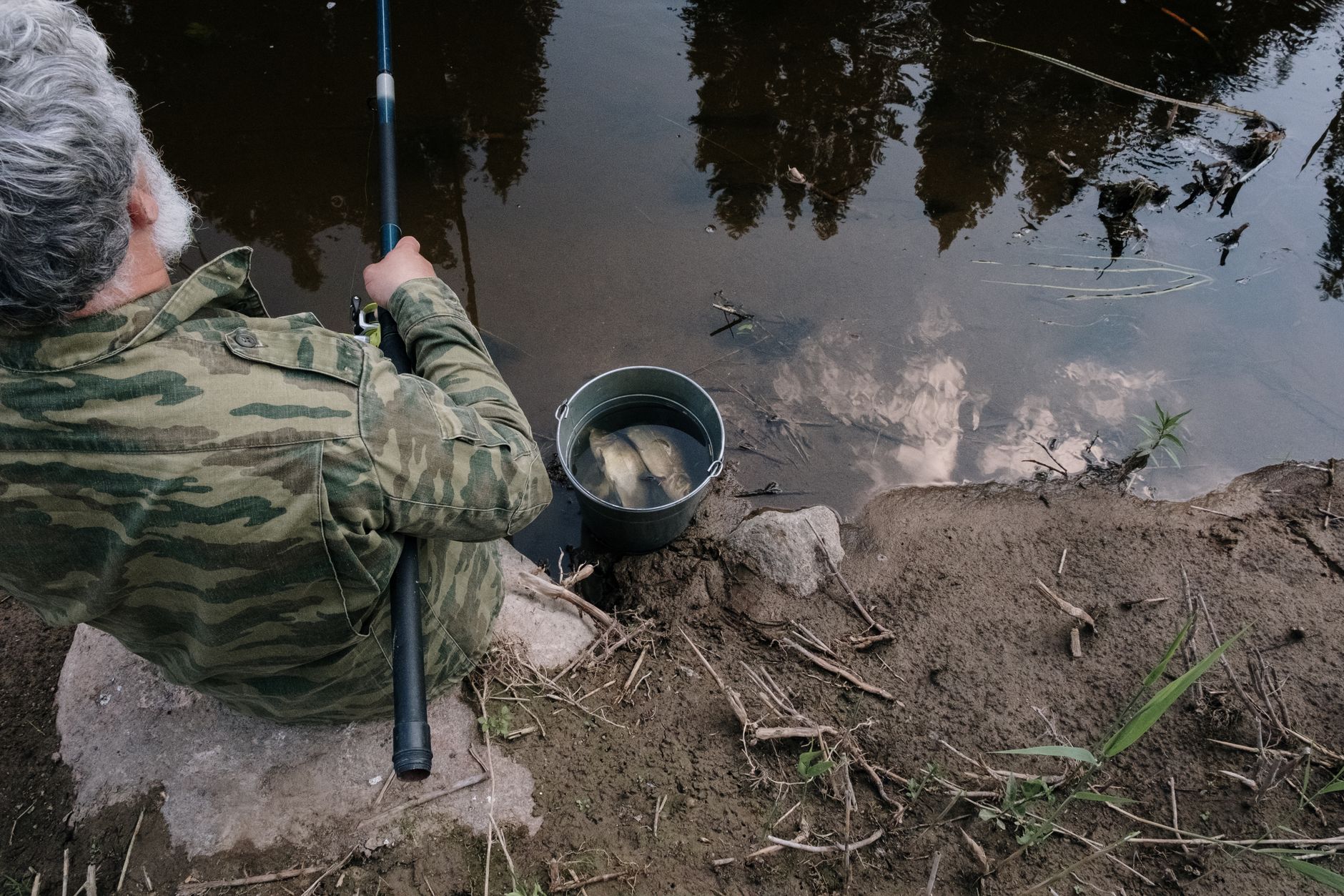 Pêcheur au coup assis au bord de l'eau avec une longue canne