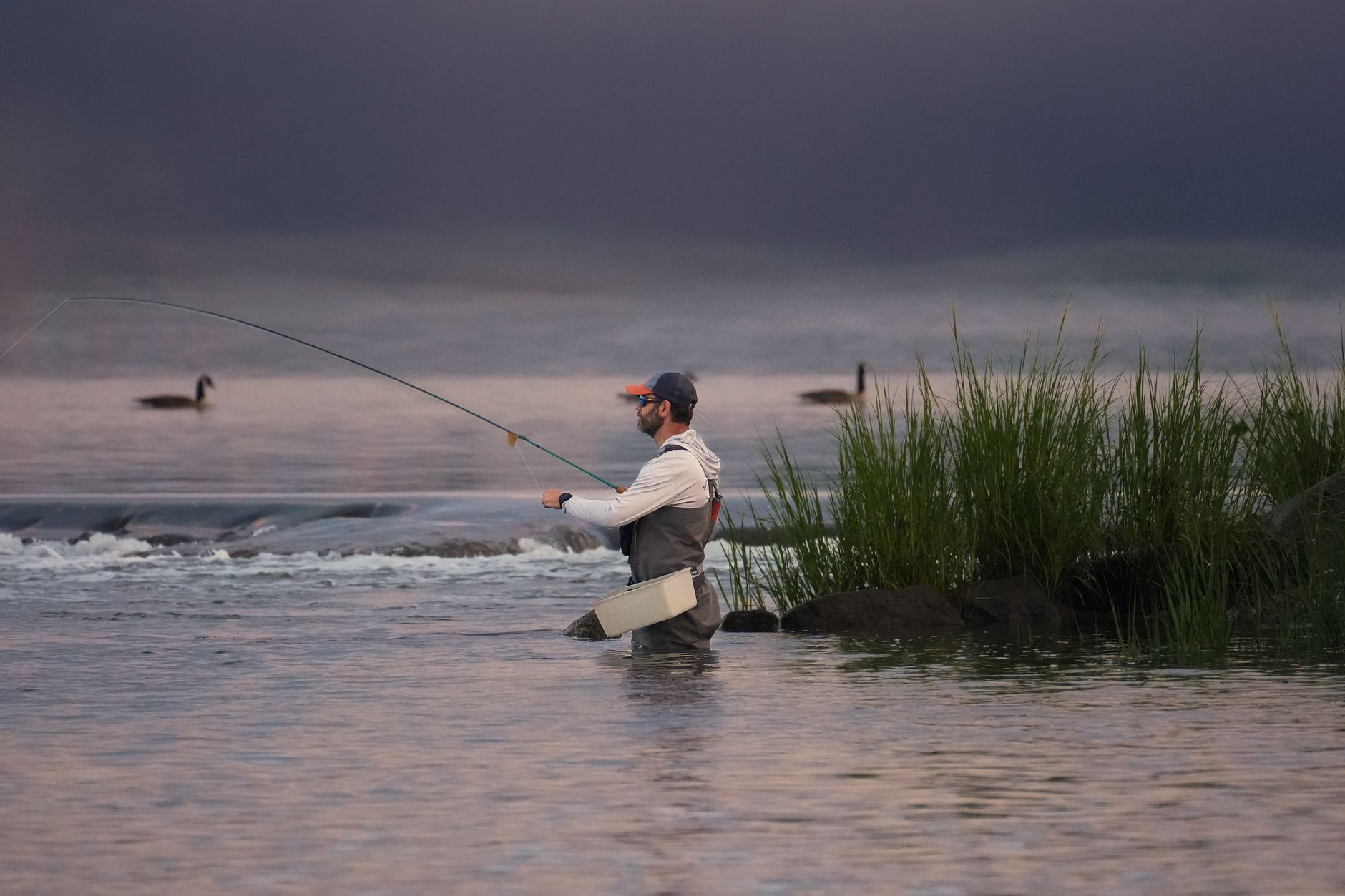 Pêcheur à la mouche debout dans l'eau à l'aube
